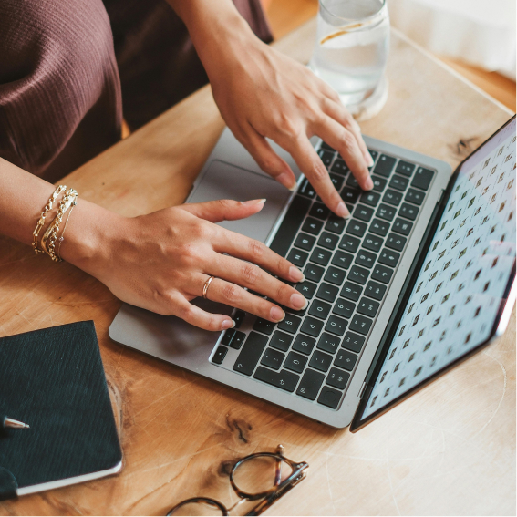 hands-typing-on-laptop-on-wooden-desk-with-notebook-and-glasses
